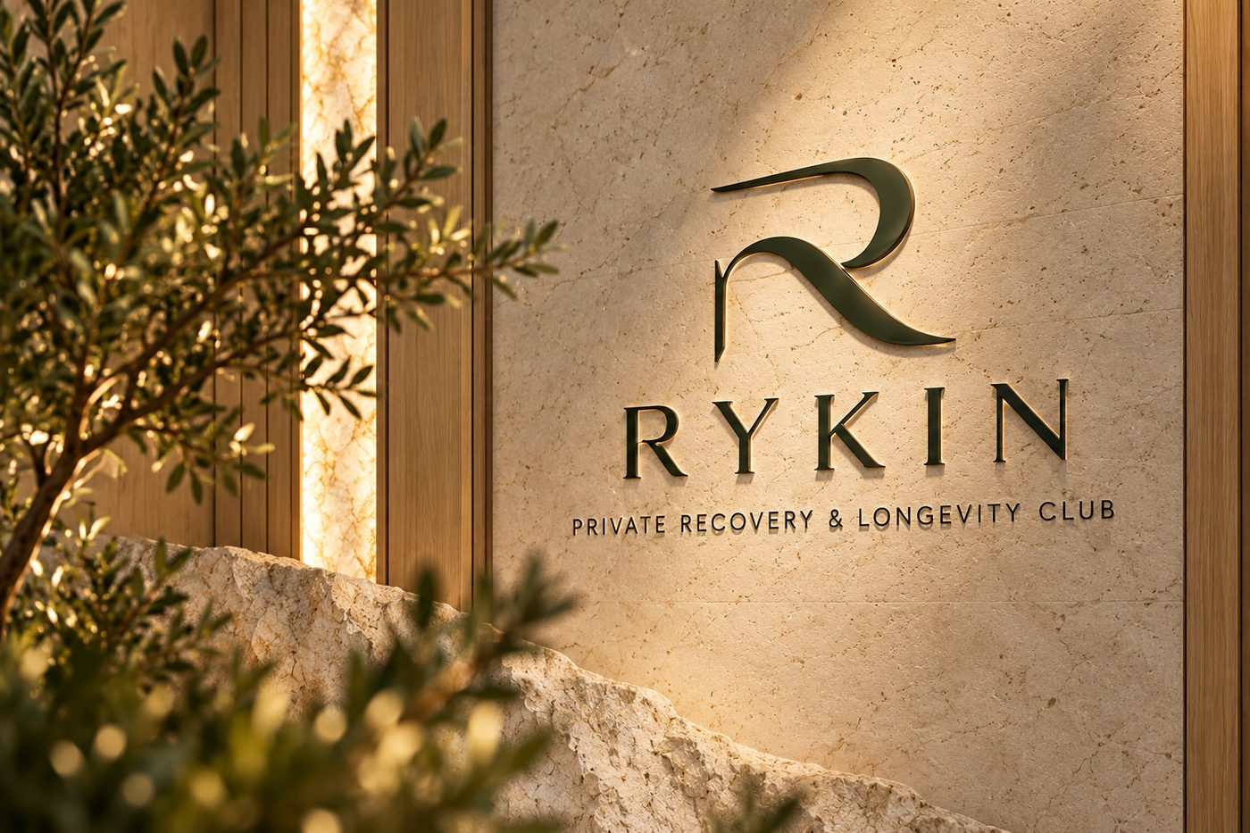 Zid od travertina s natpisom RYKIN, Private Recovery & Longevity Club, i maslinom u prvom planu